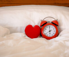 Red,alarm,clock,and,heart,shape,on,white,bed,sheet
